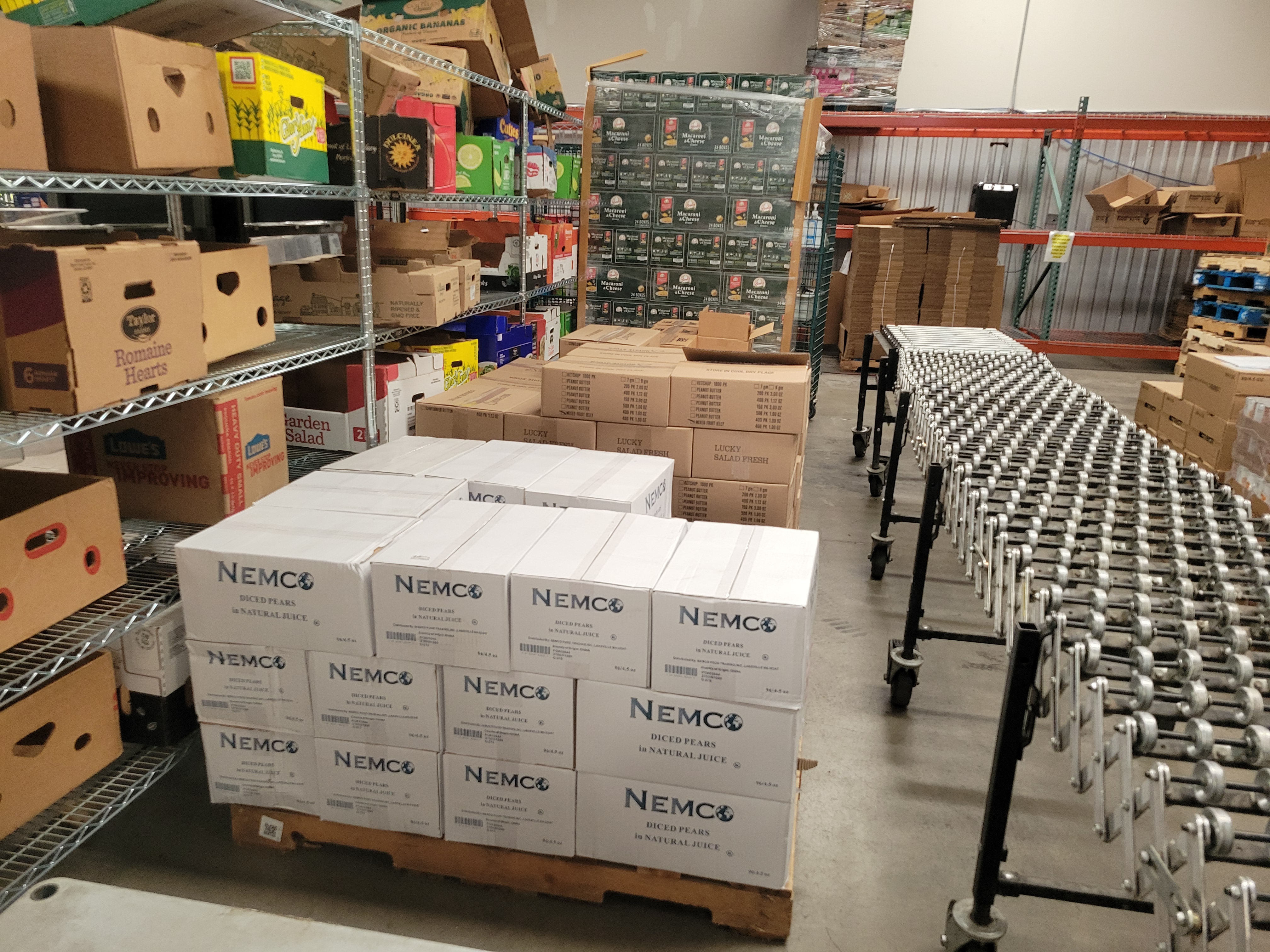 To the left is shelves full of banana boxes, to the middle is pallets of food, and to the right is a conveyor belt.